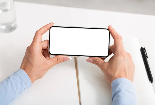 Mit dem Smartphone zur Arbeit. Weibliche Hände halten Telefon auf weißem Schreibtisch — Stockfoto