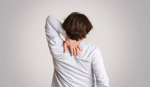 Klåda och allergier. Guy repor ryggen med handen isolerad på grå bakgrund — Stockfoto