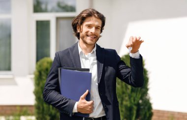 Neşeli emlakçı elinde yeni evin anahtarını tutuyor. Satılık ya da kiralık, açık havada.