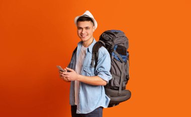 Turuncu arka planda akıllı telefon kullanan neşeli bir adam.