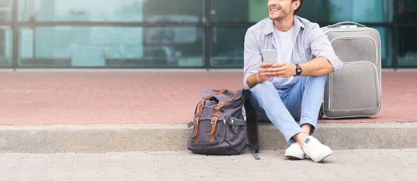 Hombre irreconocible sentado cerca de la terminal del aeropuerto con equipaje y el uso de teléfono inteligente — Foto de Stock