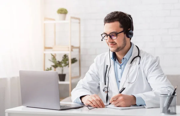 Online lektioner och konferenser. Läkaren antecknar sittande vid bordet med laptop — Stockfoto