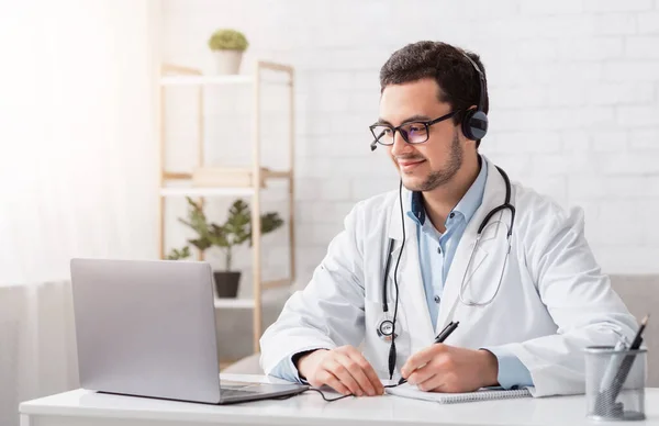 Online lessen en conferenties. Doctor maakt notities zitten aan tafel met laptop — Stockfoto