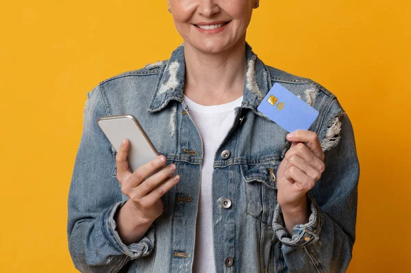 オンライン送金にスマートフォンやクレジットカードを使う中年女性の笑顔 — ストック写真