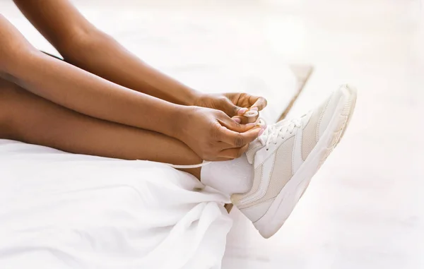 Mañana corriendo. Chica afroamericana atando cordones en zapatillas sentadas en la cama — Foto de Stock