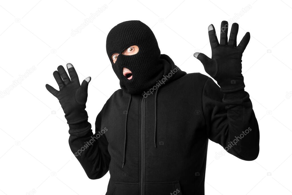 Arrested masked thief with raised arms isolated over white wall
