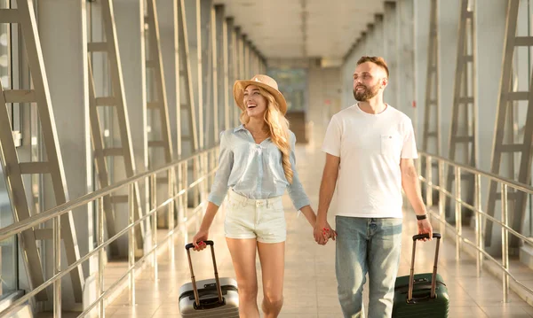Pareja feliz caminando en el aeropuerto con equipaje — Foto de Stock