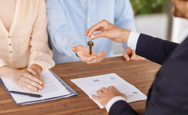 Real estate agent giving house key to young couple after signing property agreement at table, close up — Stock Photo, Image