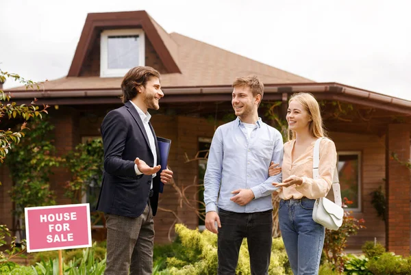 Fiatal család beszél ingatlan ügynök vásárolni ingatlan közelében gyönyörű ház kívül — Stock Fotó