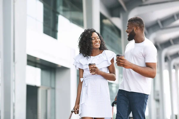 Glad svart man och kvinna promenader med kaffe nära flygplatsen byggnad — Stockfoto