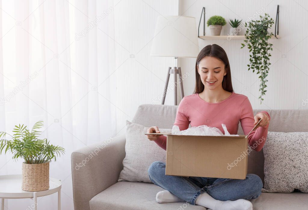 Purchase expectation. Woman opens box from online store, sitting on couch in living room