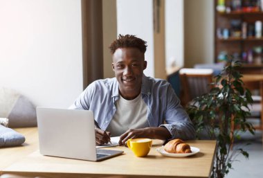 Diz üstü bilgisayarı olan Afrikalı Amerikalı öğrenci şehir kafesinde ödev yapıyor.
