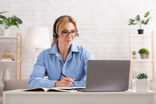 Educación en línea en el ordenador portátil. Mujer en auriculares escribir notas, escuchar conferencia —  Fotos de Stock