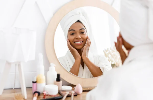 Cuidados com a pele. Jovem bela mulher negra tocando seu rosto perto do espelho — Fotografia de Stock