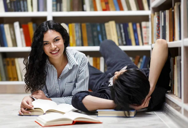 Dos estudiantes multiculturales tumbados en el piso de la biblioteca del campus —  Fotos de Stock