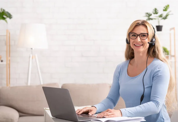 Chat en línea con el cliente. Mujer de mediana edad con auriculares se sienta a la mesa con el ordenador portátil — Foto de Stock