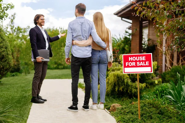 Corretor imobiliário mostrando casa para venda ao jovem casal, fora — Fotografia de Stock