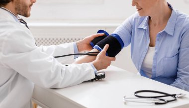 Ofisteki yaşlı kadının tansiyonunu ölçen doktor.