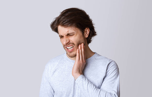 Tooth disease. Man feels pain, grimaces and press hand to cheek