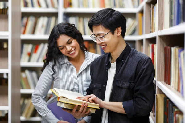 Sorrindo casal de estudantes multiculturais em pé na biblioteca moderna — Fotografia de Stock