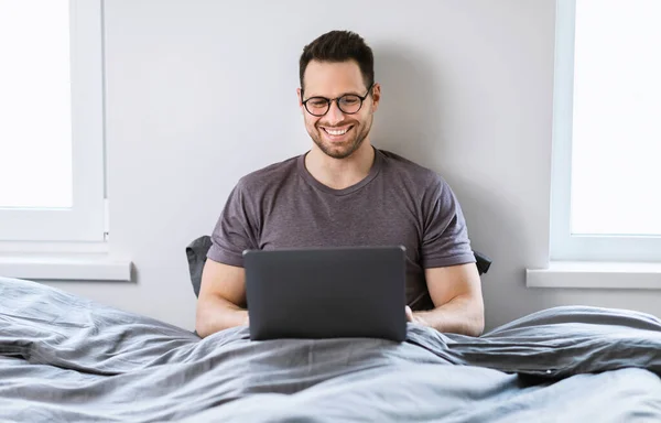 Happy Man pracuje na laptopie siedzi w łóżku w domu — Zdjęcie stockowe