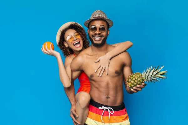 Summertime. Cheerful african couple in swimwear with tropical fruits in hands