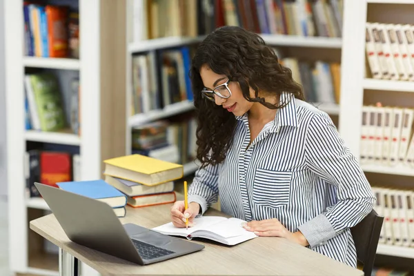 Latina dziewczyna robi pracę domową siedzi w biurku w bibliotece — Zdjęcie stockowe