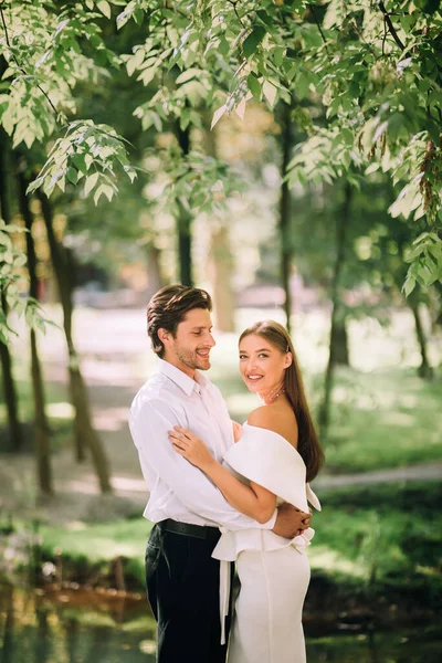 Pareja recién casada de pie abrazando al aire libre en el parque natural, tiro vertical — Foto de Stock