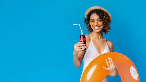 KHARKIV, UKRAJNA - Március 31. 2019: Pozitív afrikai lány Coca-Cola Classic frissítő ital szalmával kék alapon — Stock Fotó