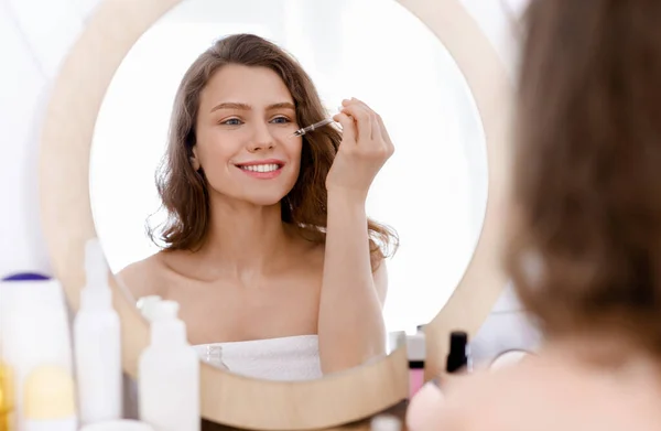 Молодая женщина применяет косметическую сыворотку в ванной комнате — стоковое фото