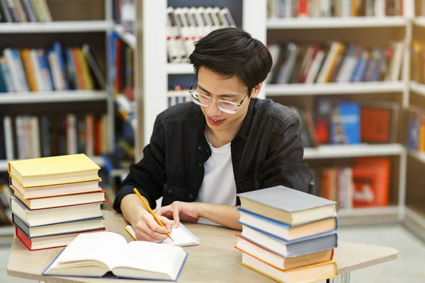 Lern- und Bildungskonzept. Asiatische männliche Studenten schreiben in Notizblock in öffentlicher Bibliothek, Hausaufgaben machen, Kopierraum — Stockbild Asiatisch guy doing hometask sitting bei schreibtisch im bibliothek — Stockfoto