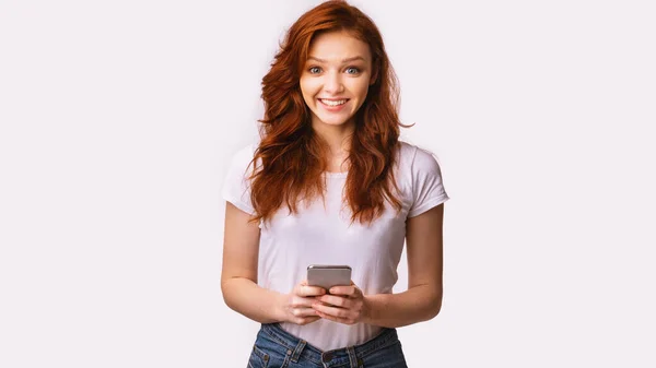Chica feliz Millennial usando Smartphone de pie sobre fondo de estudio blanco — Foto de Stock