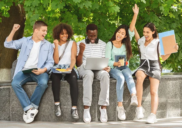 Resultados del examen universitario. Estudiantes emocionados mirando el portátil, celebrando el éxito al aire libre —  Fotos de Stock