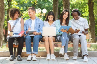 Sınavlara birlikte çalışan, dışarıda bankta oturan çok ırklı arkadaşlar.
