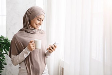 Sabah Gevşemesi. Ev Penceresi Yakınındaki Kahve ve Cep Telefonu Olan Arap Kadın