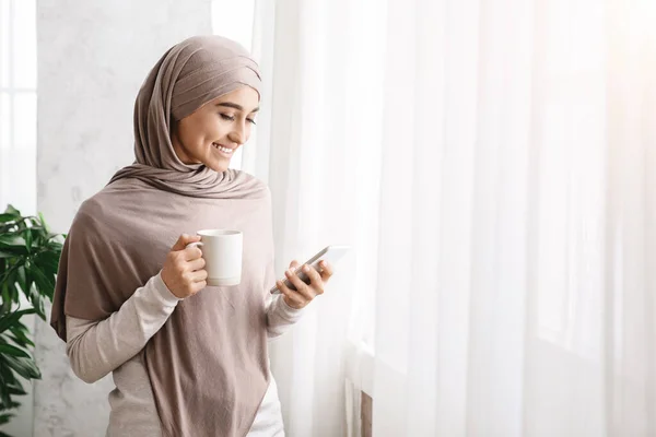 Relaksasi Pagi. Wanita Arab Dengan Kopi dan Cellphone Dekat Jendela Di Rumah — Stok Foto