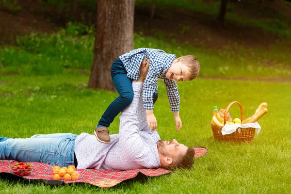 Pasillos familiares al aire libre. Padre joven jugando con su pequeño hijo divertido durante el picnic al aire libre, espacio libre — Foto de Stock