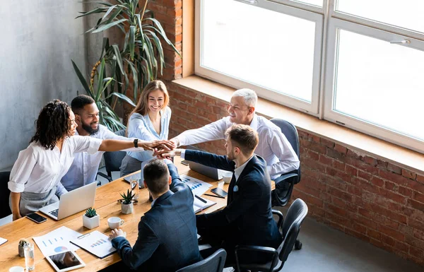 Об "єднана команда бізнесу тримає руки, сидячи разом у сучасному офісі — стокове фото