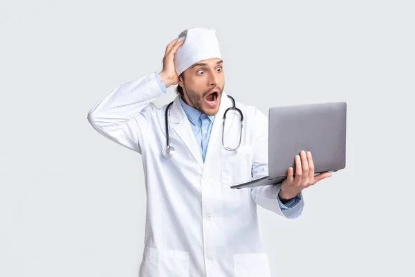 Shocked young doctor looking at laptop in amazement Royalty Free Stock Photos