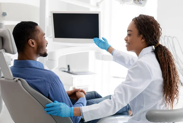 Dentista africana feminina apontando para exibição em branco, mostrando algo paciente — Fotografia de Stock