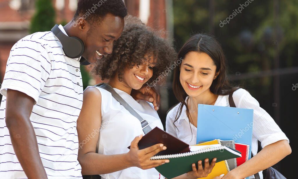 Cheerful students studying outdoors, standing in college campus, checking classes schedule