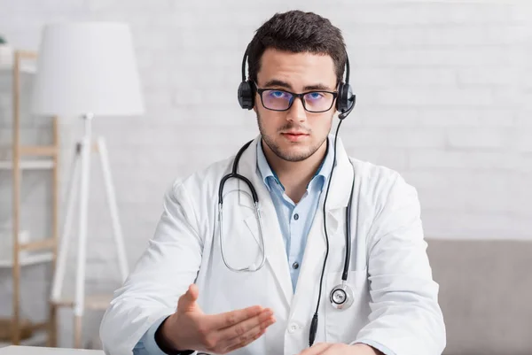 Dokter advies of online webinar. Serieuze dokter in bril en koptelefoon legt iets uit — Stockfoto