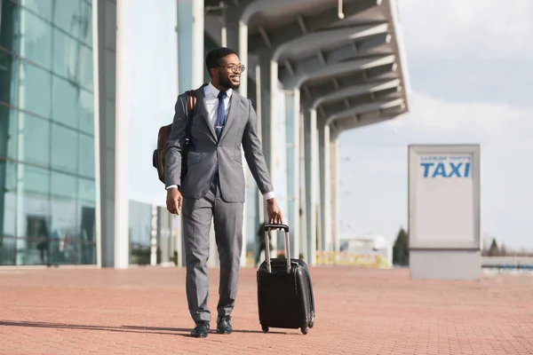 Feliz empresario africano que llega al aeropuerto caminando con la maleta al aire libre — Foto de Stock