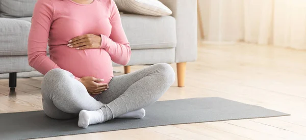无法辨认的怀孕黑人妇女坐在健身垫上，摸着肚子 — 图库照片