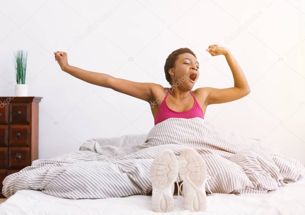 Ready for sport. Yonge woman in running shoes in bed wakes up and yawns