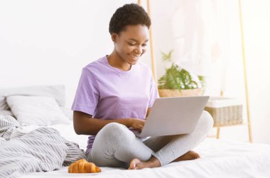 Uzaktan çalışma ve evden webinar izleme. Kız dizüstü bilgisayarla yatakta oturuyor.