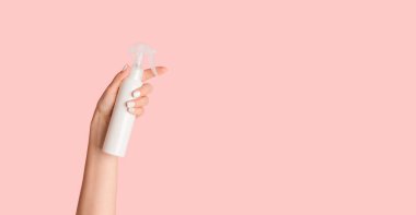 Tanımlanamayan genç bayan elinde beyaz sprey şişesiyle pembe arka planda, boş alanda kozmetik ürünler tutuyor.