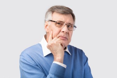 Düşünceli kıdemli beyefendi kamera pozuna bakıp, gri arkaplan...
