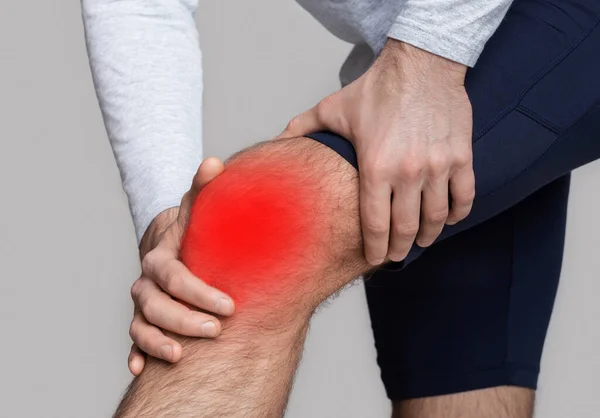 Τραυματισμός στο γόνατο ή φλεγμονή. Ο άνδρας με αθλητικά πιέζει τα χέρια του στο γόνατο τονίζοντας με κόκκινο. — Φωτογραφία Αρχείου