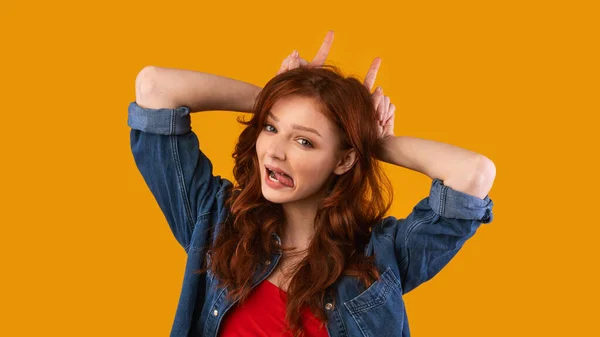 Menina adolescente mostrando chifres de touro se divertindo Grimacing, fundo amarelo — Fotografia de Stock